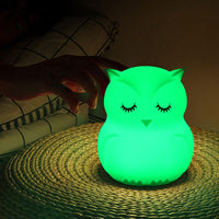 Veilleuse hibou à LED éclairée en vert, posée sur une table de chevet