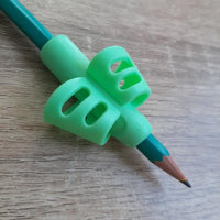 Gros plan du guide doigt vert placé sur un crayon, aidant à corriger la préhension et la posture d’écriture.

